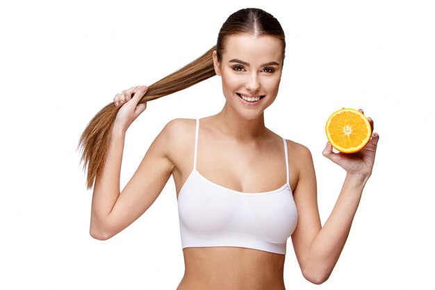 Портрет привлекательной улыбающейся женщины, держащей апельсин на белом фоне