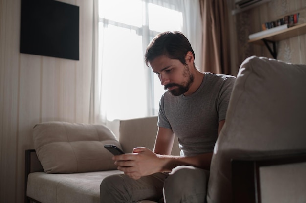 Portrait of an attractive smiling young bearded man wearing casual clothes sitting on a couch