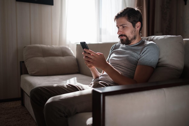 Portrait of an attractive smiling young bearded man wearing casual clothes sitting on a couch