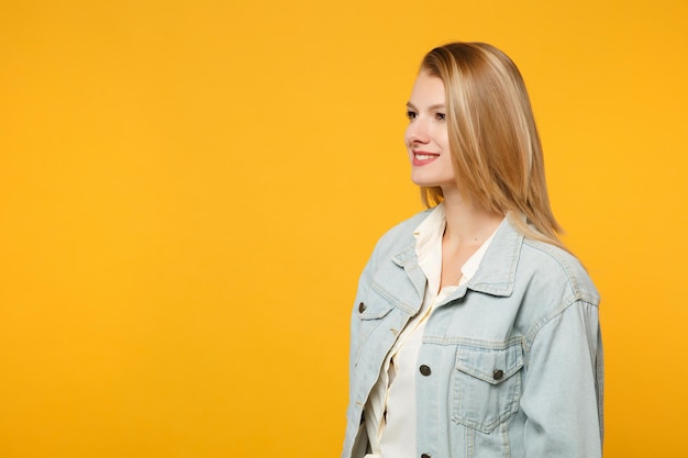 Portrait of attractive smiling young woman in denim casual clothes standing and looking aside isolated on bright yellow orange wall background in studio. people lifestyle concept. mock up copy space