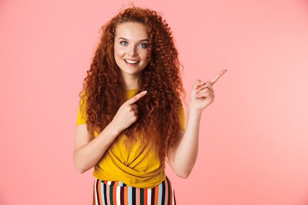 Portrait of an attractive smiling young woman with long curly red hair standing isolated, presenting copy space