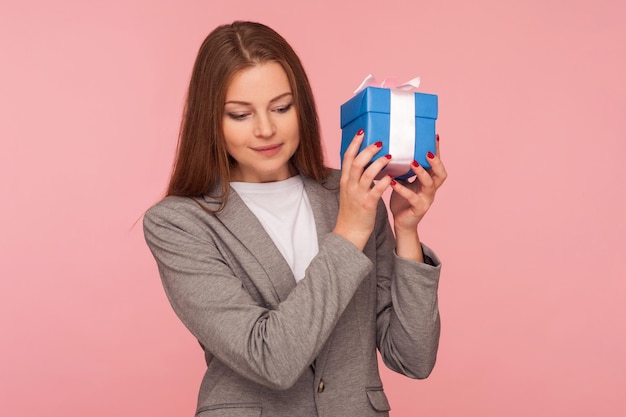 Portrait of attractive stylish businesswoman in suit jacket holding elegant small gift congratulation on birthday giving present on Valentine39s day indoor studio shot isolated on pink background