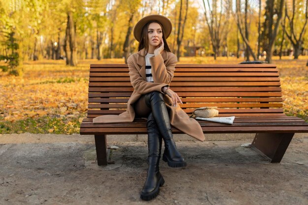 Photo portrait of attractive stylish smiling portrait of attractive stylish smiling woman with long hair walking in the park dressed in warm brown coat autumn trendy fashion street style wearing hat