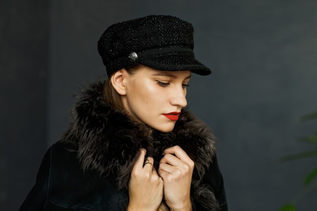 Portrait of attractive woman in a black cap and a coat with a fur collar