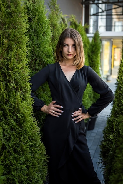 Portrait of attractive woman in black fashion dress near thuja occidentalis trees lifestyle