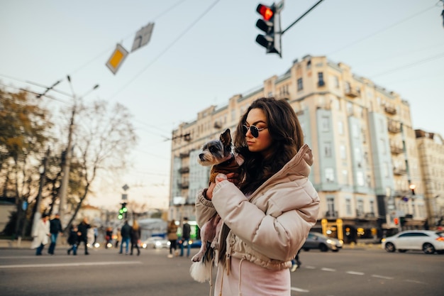 Portrait of attractive woman in casual clothes on city street with dog in hands looking aside