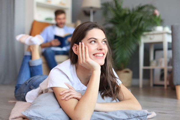 Portrait of attractive woman relaxing on floor with blurred man in background.