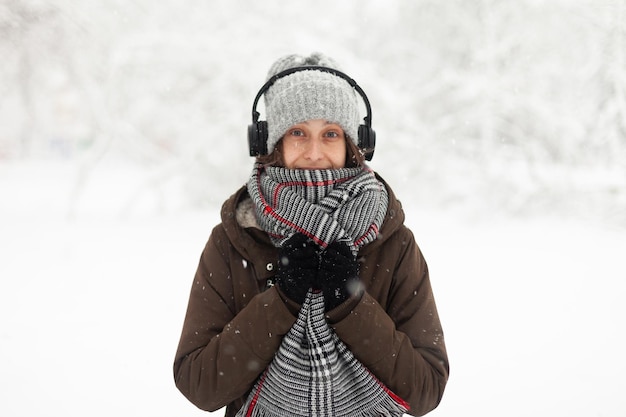 冬の雪の屋外で暖かい服を着た魅力的な女性の肖像画は、ヘッドフォンで音楽を聴く