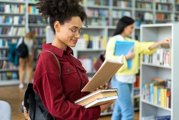 Photo portrait of attractive woman with books in hands in beautiful public library posing at camera with calm face female student reads books in the student library