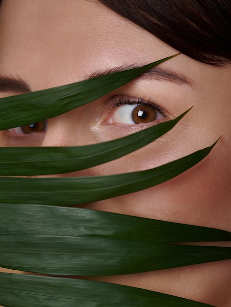 portrait of attractive woman with expressive eyes and covering half of her face with palm leaf