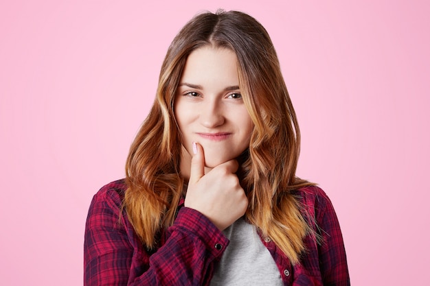 Portrait of attractive woman with intriguing expression keeps hand under chin