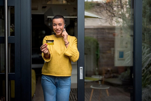 Portrait of attractive young adult woman talking on the phone holding credit card