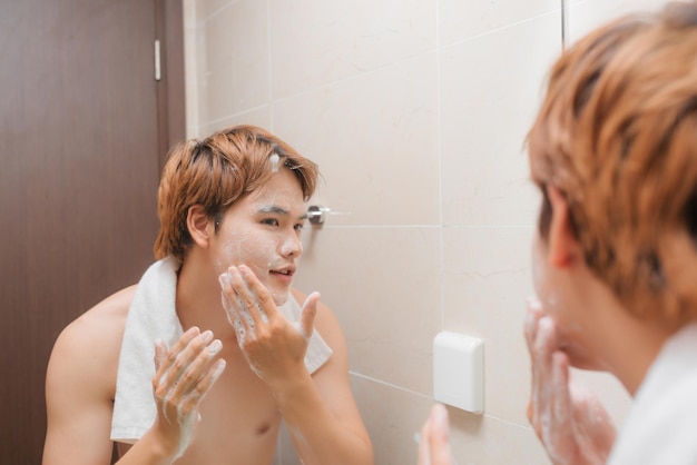 魅力的なアジアの若い男性の肖像画は、バスルームで顔を洗う