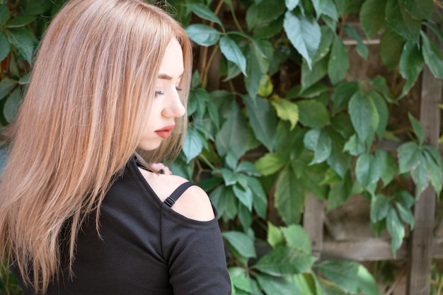 Portrait of attractive young blonde woman in black blouse profile Green plants background Beautiful girl