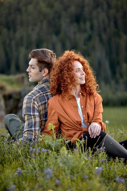 Portrait of attractive young caucasian couple sitting back to back to each other on grass relaxing i...