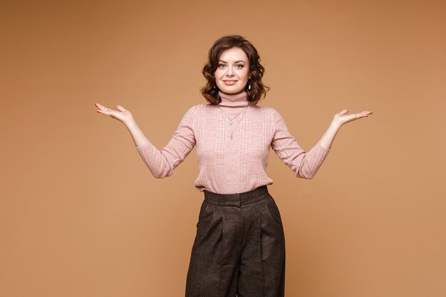 Portrait of attractive young caucasian female with short dark wavy hair in white blouse, black trousers doesn't know what to do