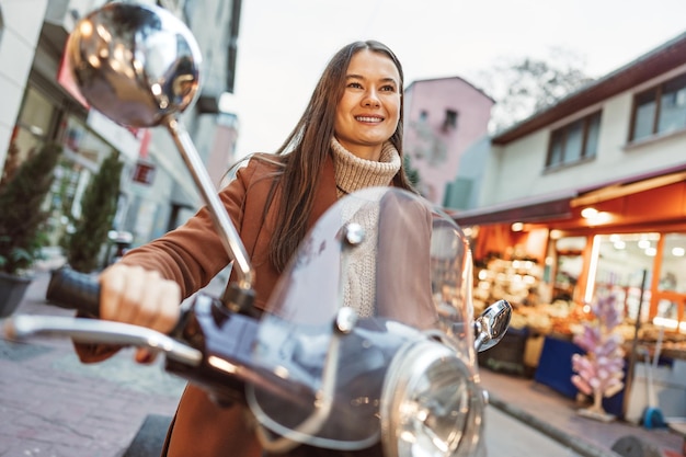 Portrait of attractive young cheerful woman riding moped scooter