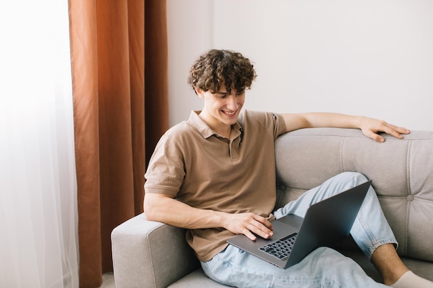 Portrait of attractive young curly hair man using laptop while sitting on sofa at home