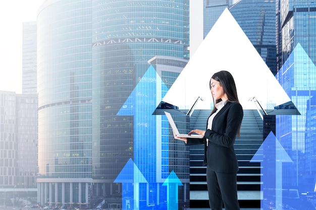 Portrait of attractive young european businesswoman with laptop\
on abstract city background with staircase mock up place and arrows\
career growth and success concept double exposure