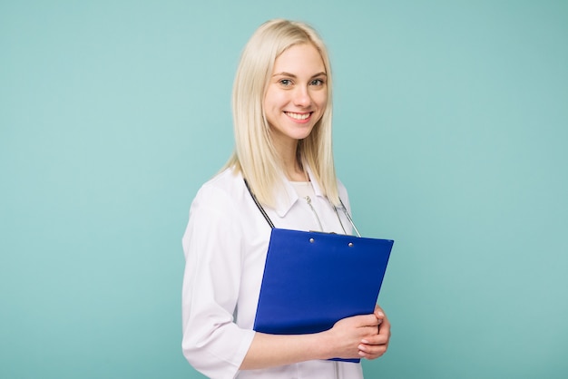 Portrait of an attractive young female doctor in white coat on blue space