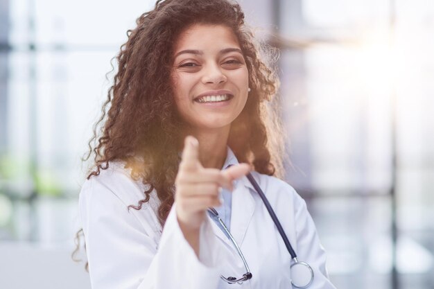 Portrait of an attractive young female doctor in a white coat points her finger