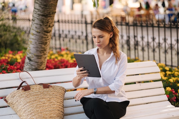 Photo portrait of attractive young lady in forma outfit sitting on bench in centre of city and using