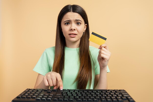 Photo portrait of attractive young latin teen girl holding credit card using keyboard isolated on beige background concept of online shopping banking