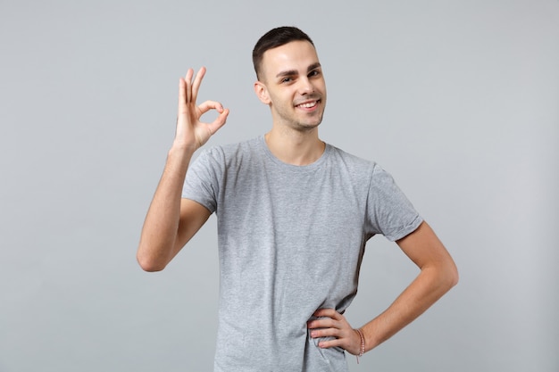 Портрет привлекательного молодого человека в повседневной одежде стоя, показывая жест ОК