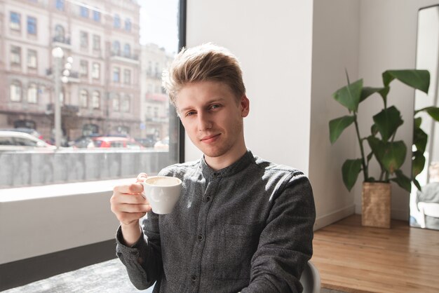 Portrait of an attractive young man in a light cozy cafe with a cup of coffee