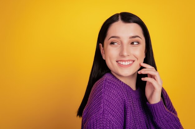 Portrait of attractive young woman happy positive smile hand touch cheek look empty space isolated over yellow background