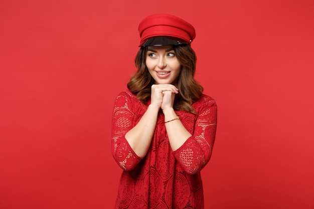 Portrait of attractive young woman in lace dress and cap looking aside, put hand prop up on chin isolated on bright red wall background. People sincere emotions, lifestyle concept. Mock up copy space.