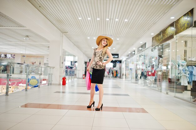 Portrait of an attractive young woman in leopard blouse, black skirt posing with a hat and shopping bags