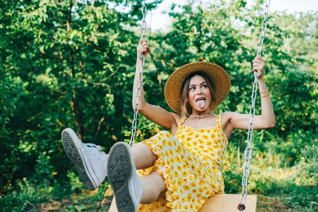 Portrait of attractive young woman in straw hat outdoors in summer sunny day on a swing.