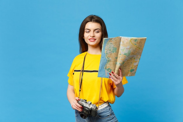 Portrait of attractive young woman in vivid casual clothes with retro vintage photo camera hold paper city map isolated on blue wall background in studio. People lifestyle concept. Mock up copy space.