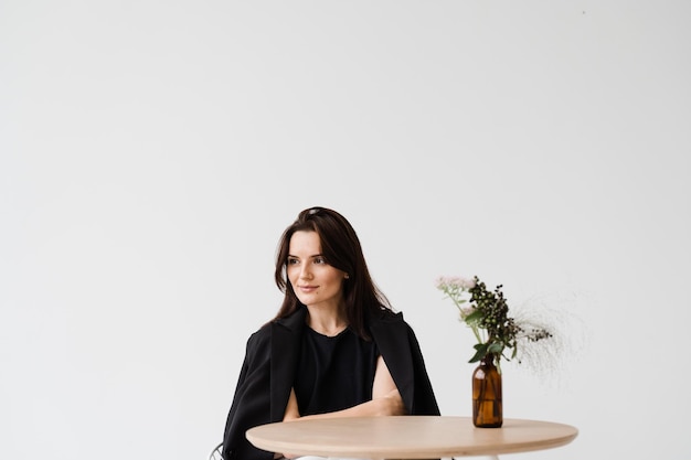 Portrait of attractive young woman on white background dreamy\
cheerful girl dressed in business style is sitting at table in\
white cafe