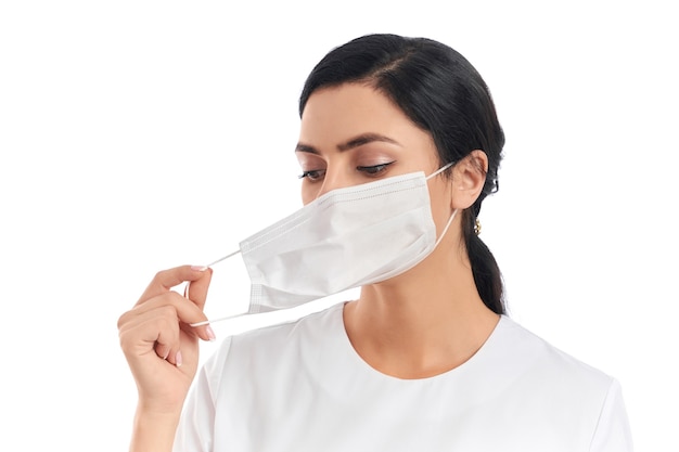 Portrait of attractive young woman with dark hair getting off medical protective mask on white