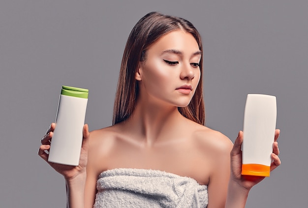 Portrait of attractive young woman with two shampoos on grey\
background. making choice. women care