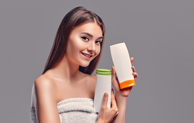 Portrait of attractive young woman with two shampoos on grey\
background. making choice. women care