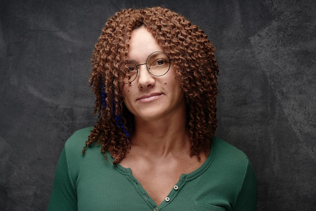 Portrait of an authentic adult woman with afro curls against a black wall in the studio. Unusual stylish woman with red hair
