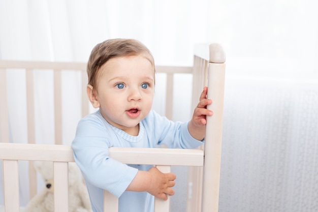 Portrait of a baby boy in a crib in a children's room with big blue eyes