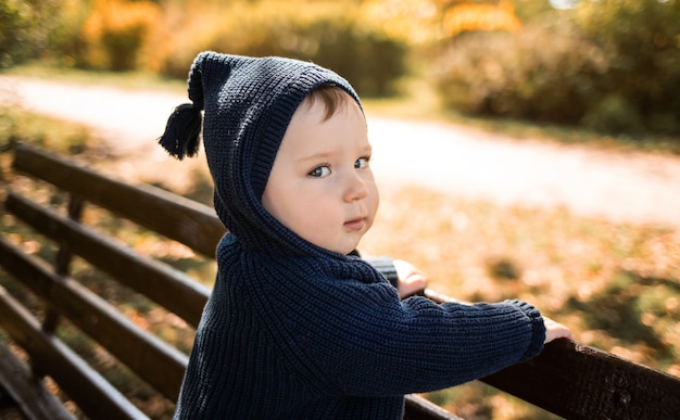 Portrait of a baby boy in a hood holding a bench. Autumn walks.