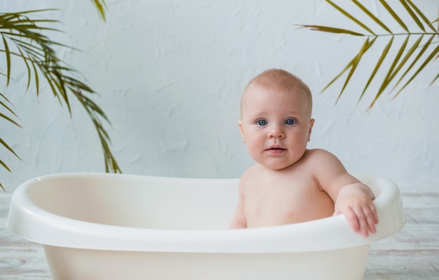 Portrait of a baby boy sitting in a white bath on a white surface with space for text