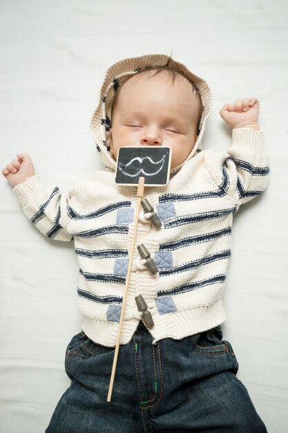 Photo portrait of baby boy with decorative mustaches lying on bed