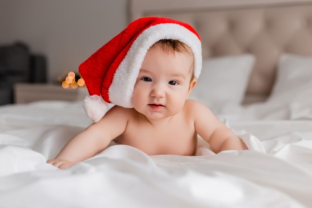 portrait of a baby in diaperspanties and a Santa Claus hat lying on his stomach on a white sheet