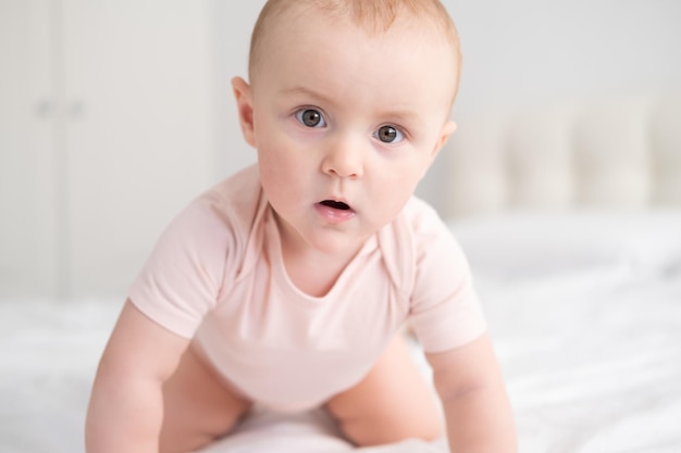 Portrait of baby girl  months in light pink bodysuit on white bedding on bed