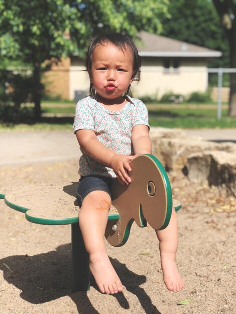 Foto ritratto di una bambina seduta su attrezzature da gioco al parco giochi