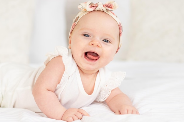 Portrait of a baby girl smiling or laughing lying on a white cotton bed at home