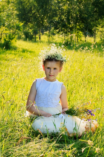 Portrait of a baby girl on a summer meadow with a bouquet of wildflowers in his hand