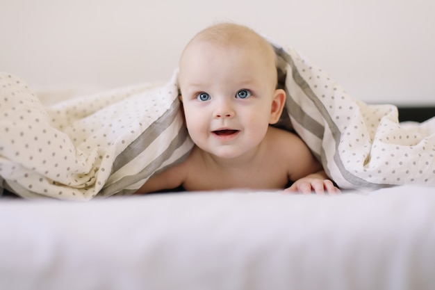 portrait of baby hiding under the blanket in bed