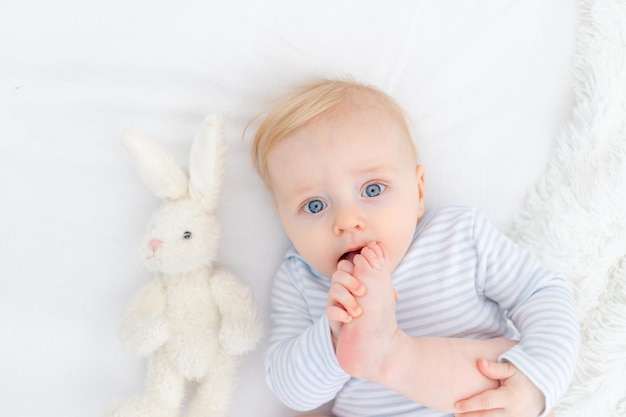 Portrait of baby sucking foot lying on bed baby boy blonde six months